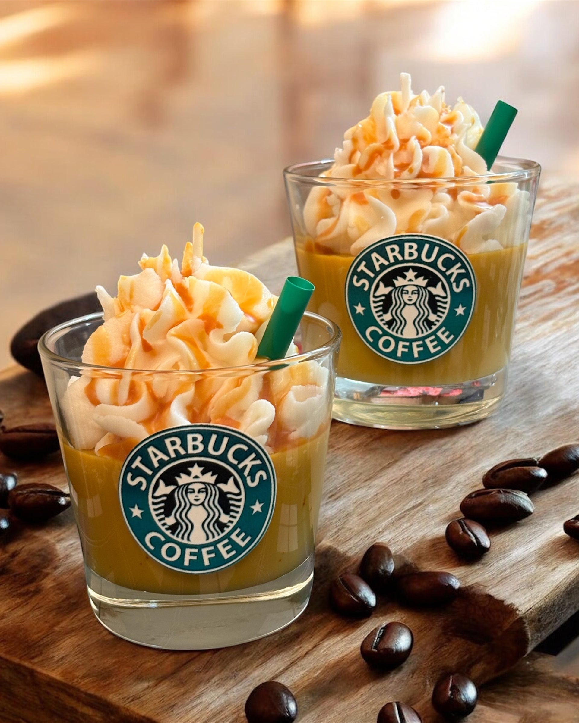 Two Starbucks coffee drinks with whipped cream and a straw on a wooden surface with scattered coffee beans.